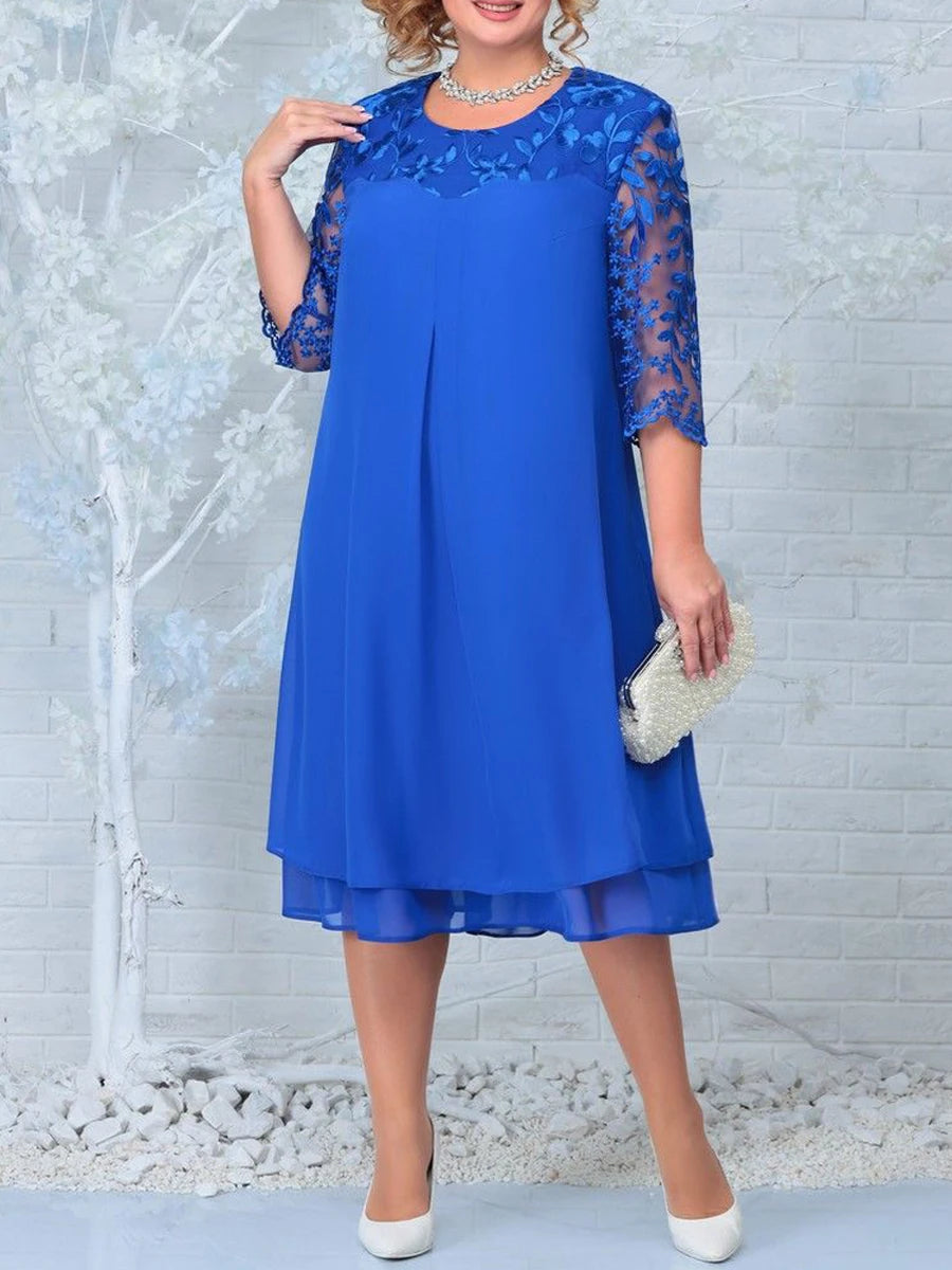 Woman wearing a blue dress with lace sleeves against a light brick wall.