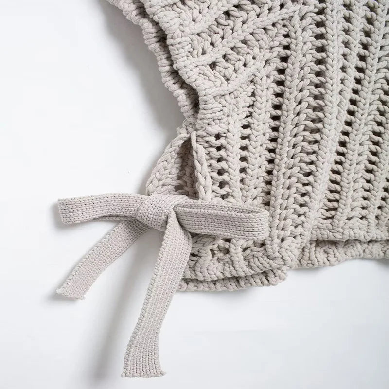 Close-up of a beige knitted baby romper with a bow on a white background