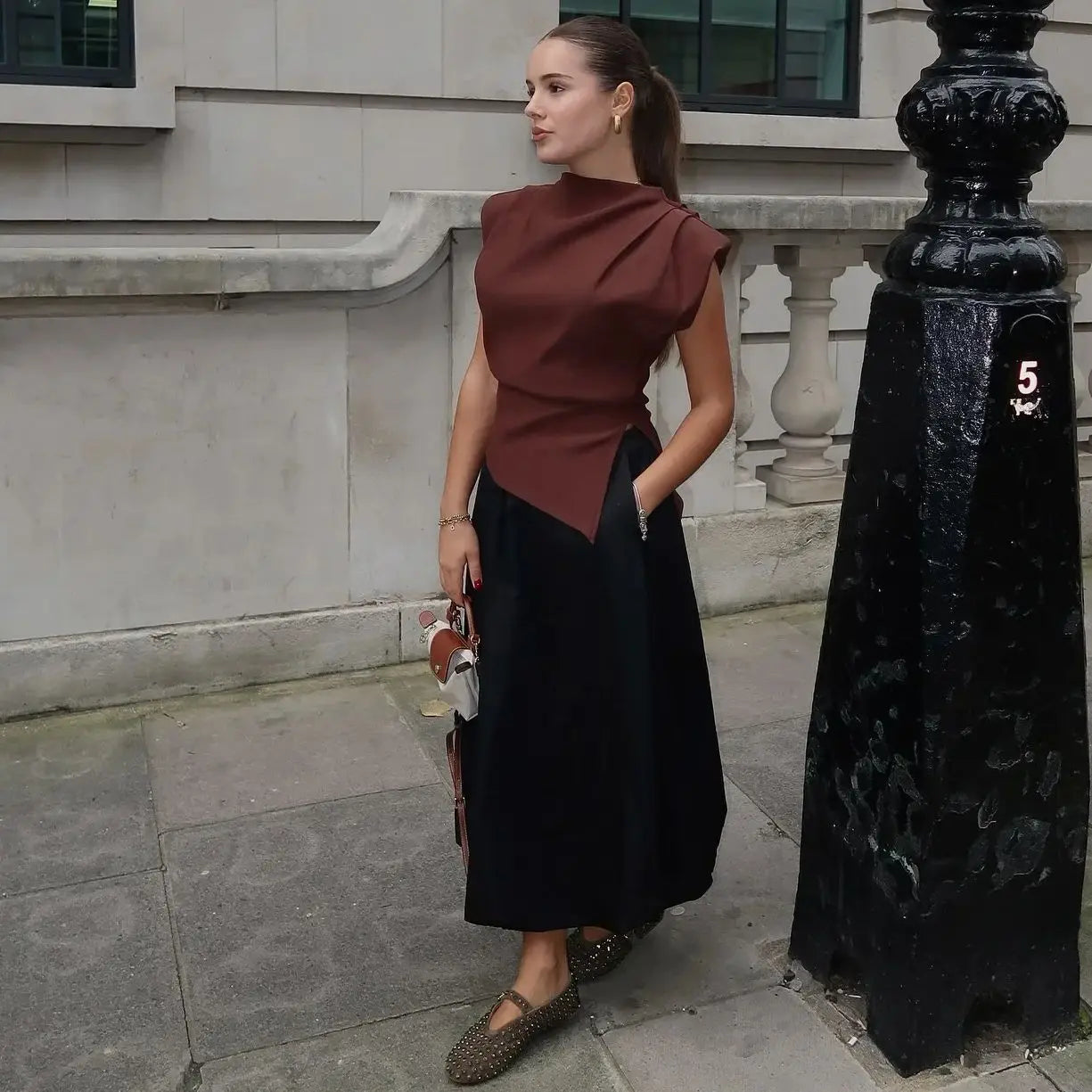 Woman in a brown top and black skirt standing on a city street.
