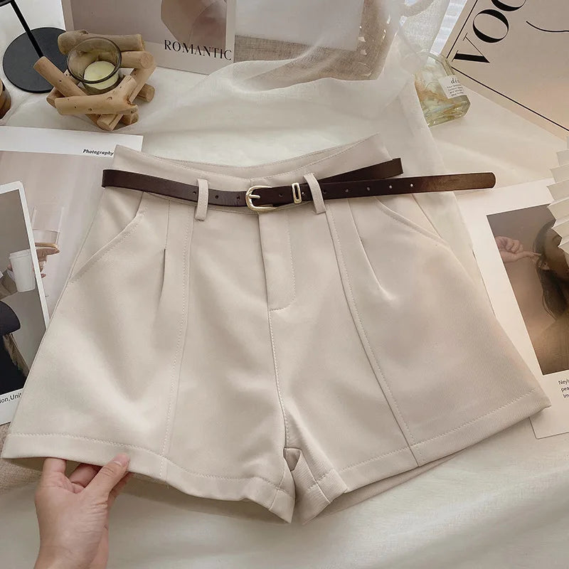 Beige shorts with a brown belt on a surface with magazines and decor items.