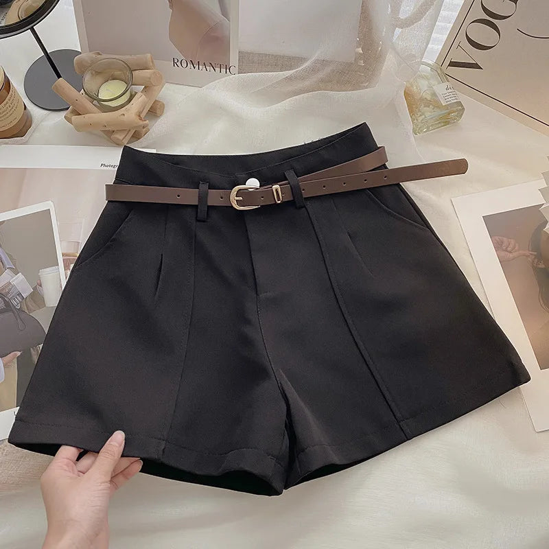 Black shorts with a brown belt held by a hand on a light surface.