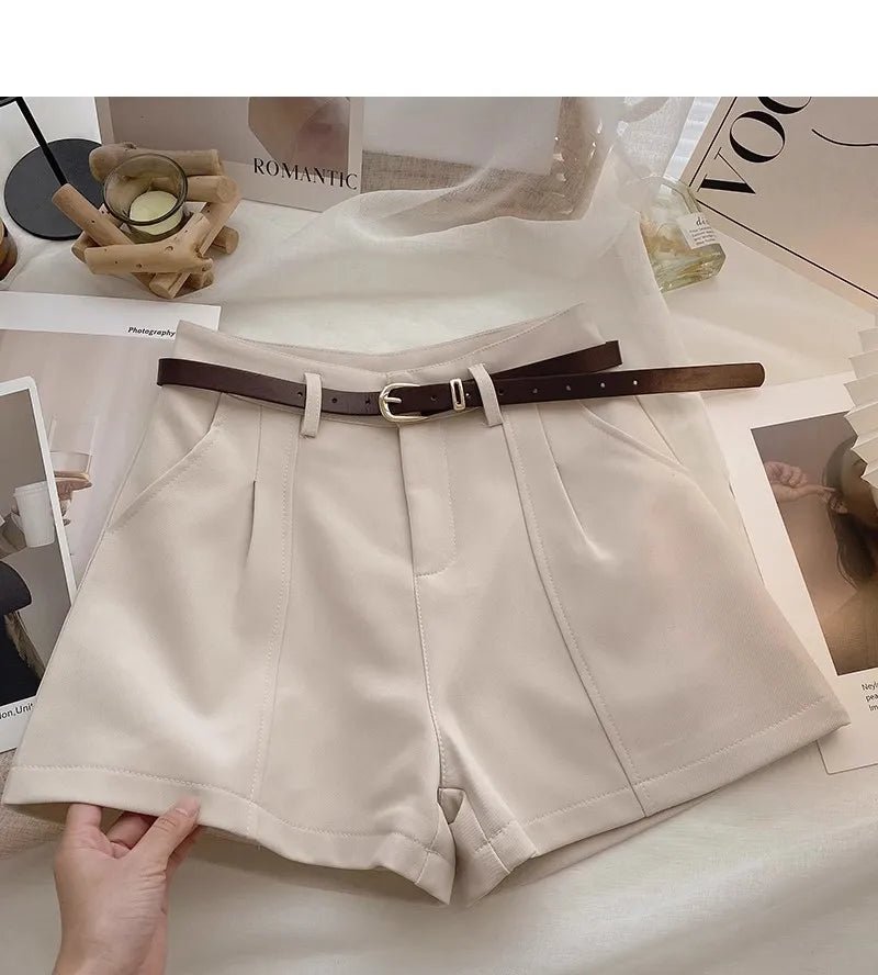 Beige shorts with a brown belt on a surface with magazines in the background.